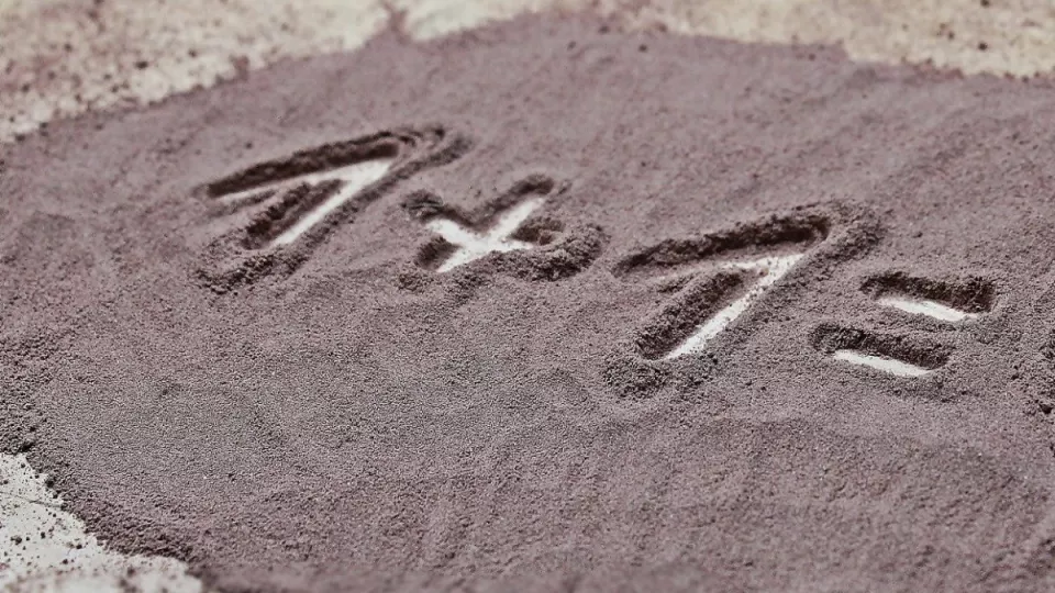 räkneuppgift "1 + 1 =" skrivet i sand. Foto.